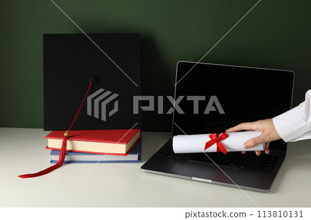 A graduate's hat on a laptop, on a green background. 113810131