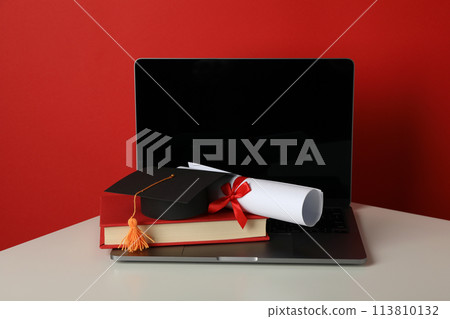 Graduate hat with diploma, book and laptop on red background. 113810132