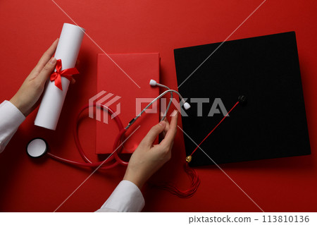 Graduate hat with diploma and stethoscope, on red background. Graduate hat with diploma and stethoscope, on red background. 113810136