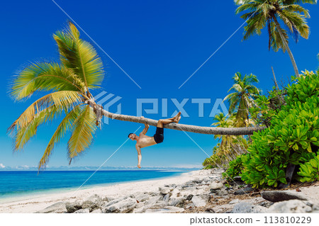 Man shirtless on the beach and climbs a coconut palm tree. Slim man vacation on paradise beach 113810229