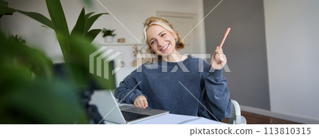 Portrait of young smiling woman, student talking to teacher online via video chat, doing course, attends remote course in internet, making notes Portrait of young smiling woman, student talking to teacher online via video chat, doing course, attends remote course in internet, making notes 113810315