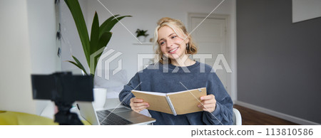 Portrait of smiling blond woman, sitting in bedroom, using laptop and digital camera, recording video for lifestyle blog, reading, using her notebook Portrait of smiling blond woman, sitting in bedroom, using laptop and digital camera, recording video for lifestyle blog, reading, using her notebook 113810586