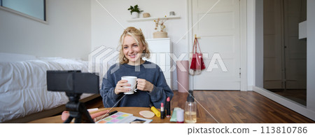 Portrait of beautiful social media beauty blogger, sitting in front of digital camera on floor in bedroom, drinking tea and chatting, talking to followers Portrait of beautiful social media beauty blogger, sitting in front of digital camera on floor in bedroom, drinking tea and chatting, talking to followers 113810786