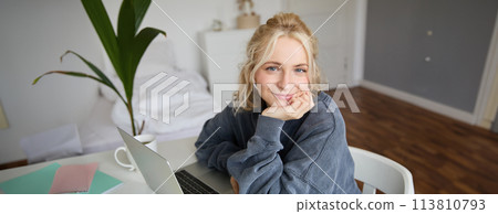 Portrait of young smiling woman, female student sitting in her room with laptop, looking cute at camera Portrait of young smiling woman, female student sitting in her room with laptop, looking cute at camera 113810793