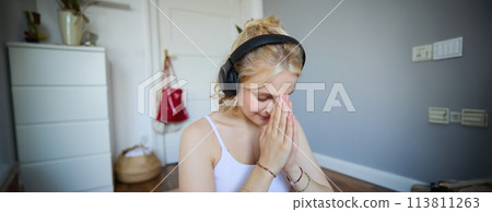 Close up portrait of young sporty woman in headphones, finish yoga training session, bowing with namaste hand sign, meditating Close up portrait of young sporty woman in headphones, finish yoga training session, bowing with namaste hand sign, meditating 113811263