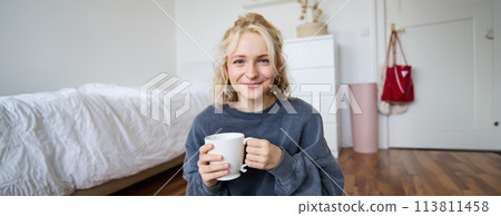 Image of young teenage girl sitting in her bedroom on floor, drinking cup of tea and enjoying day at home, smiling and looking at camera Image of young teenage girl sitting in her bedroom on floor, drinking cup of tea and enjoying day at home, smiling and looking at camera 113811458