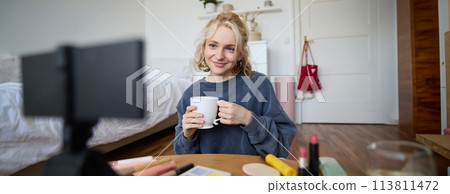 Portrait of cute blond woman, video content maker, vlogger recording on digital camera in bedroom, drinking cup of tea and talking to audience Portrait of cute blond woman, video content maker, vlogger recording on digital camera in bedroom, drinking cup of tea and talking to audience 113811472