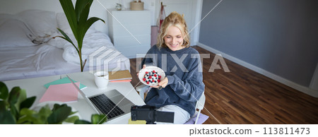 Portrait of cute young girl vlogger, showing her breakfast on camera, recording vlog in her bedroom, holding dessert, eating Portrait of cute young girl vlogger, showing her breakfast on camera, recording vlog in her bedroom, holding dessert, eating 113811473