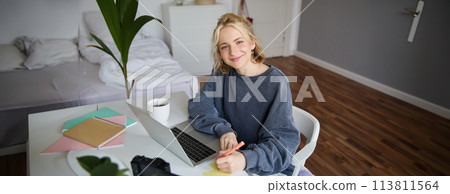 Portrait of smiling young woman, female student, doing distance learning course, using laptop, studying at home, writing down, making notes Portrait of smiling young woman, female student, doing distance learning course, using laptop, studying at home, writing down, making notes 113811564