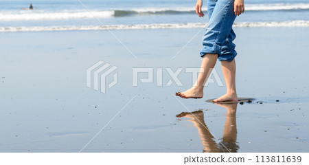 A woman walking barefoot on the beach 113811639