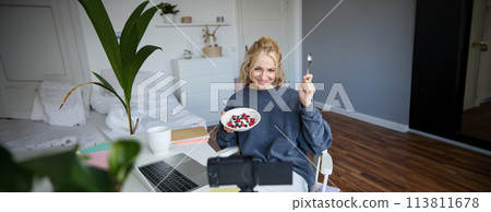 Portrait of cute young girl vlogger, showing her breakfast on camera, recording vlog in her bedroom, holding dessert, eating Portrait of cute young girl vlogger, showing her breakfast on camera, recording vlog in her bedroom, holding dessert, eating 113811678