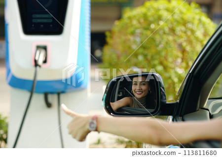 Happy ev driver showing thumbs up after charging electric car 113811680