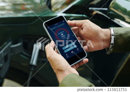 Electric car driver checking smart charger application on smartphone Electric car driver checking smart charger application on smartphone 113811731