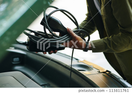 Closeup image of electric car driver putting charging cable in trunk Closeup image of electric car driver putting charging cable in trunk 113811761