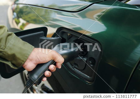 Cropped image of man inserting plug into electric car charge port Cropped image of man inserting plug into electric car charge port 113811777