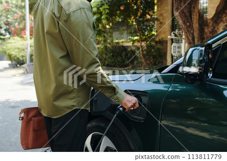 Cropped image of electric car owner inserting charging plug Cropped image of electric car owner inserting charging plug 113811779