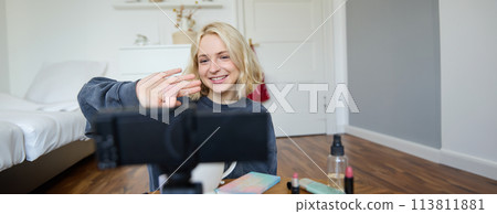 Close up portrait of happy young beauty blogger, records lifestyle vlog in her room, using camera with stabiliser, shows makeup brush and cosmetics 113811881