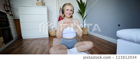 Image of sporty young woman doing workout at home, using rubber yoga mat, listening to music and exercising 113812034