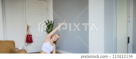 Portrait of young woman personal yoga instructor, recording workout video at home, using digital camera to vlog her exercises, using rubber mat 113812134