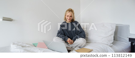 Portrait of young female student, woman studying online, e-learning on her laptop, sitting on bed with notebook and looking at screen, video chats, connects to a self-paced course Portrait of young female student, woman studying online, e-learning on her laptop, sitting on bed with notebook and looking at screen, video chats, connects to a self-paced course 113812149
