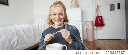 Lifestyle, beauty blogger, woman recording video of her putting on makeup, talking to camera, making online tutorial, showing her lip gloss or lipstick to followers, sitting on floor with cup of tea Lifestyle, beauty blogger, woman recording video of her putting on makeup, talking to camera, making online tutorial, showing her lip gloss or lipstick to followers, sitting on floor with cup of tea 113812387