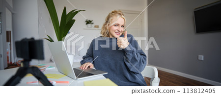 Portrait of smiling young blond woman, girl student studying from home, using online academy, doing course in internet, using laptop, showing thumbs up. Concept of distance learning 113812405
