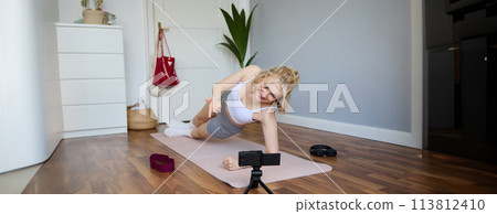 Portrait of fit and healthy young vlogger, fitness instructor woman standing in side plank, recording online lesson for clients on digital camera, shooting video about workout Portrait of fit and healthy young vlogger, fitness instructor woman standing in side plank, recording online lesson for clients on digital camera, shooting video about workout 113812410