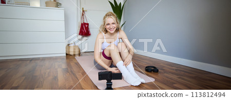 Portrait of young blond woman, social media vlogger using digital camera during workout, shooting video about exercises and fitness, stretching with rubber resistance band Portrait of young blond woman, social media vlogger using digital camera during workout, shooting video about exercises and fitness, stretching with rubber resistance band 113812494