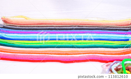 Hands touch a neatly organized rainbow of colorful, coiled clay bead strands against a contrasting white surface. Hands touch a neatly organized rainbow of colorful, coiled clay bead strands against a contrasting white surface. 113812610