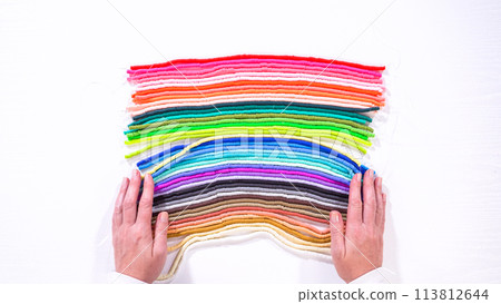 Flat lay. Artistic hands lift a selection of brightly colored clay bead cords, contrasting with organized layers beneath on a white background. 113812644
