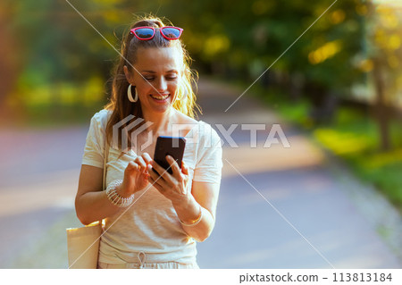 smiling trendy woman in shirt using smartphone and walking smiling trendy woman in shirt using smartphone and walking 113813184