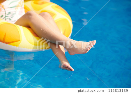 Cropped image of girl sitting in inflatable ring in swimming pool Cropped image of girl sitting in inflatable ring in swimming pool 113813189
