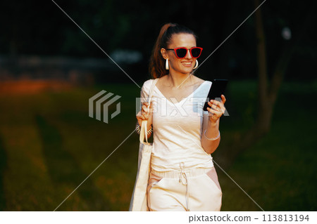 smiling elegant female in white shirt with smartphone walking smiling elegant female in white shirt with smartphone walking 113813194