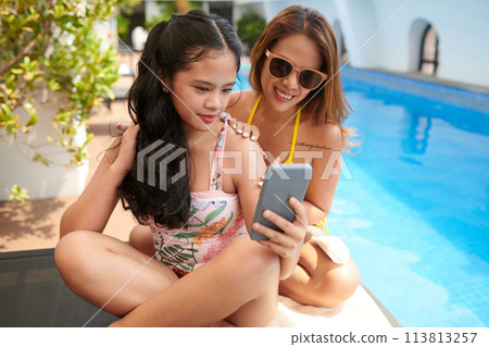Smiling teenage girl taking selfie with mother by pool 113813257