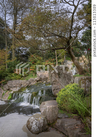 Waterfall in Kyoto Garden, a Japanese garden in Holland Park, London, UK. Holland Park is a public park with woods and gardens in the London borough of Kensington. 113813389