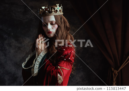 medieval queen in red dress with crown praying 113813447