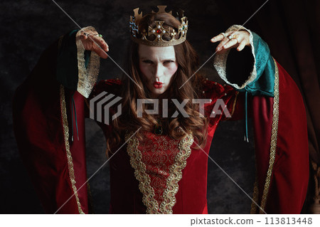 scary medieval queen in red dress with white makeup and crown 113813448