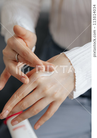 Woman applying hand cream at home, closeup Woman applying hand cream at home, closeup 113814034