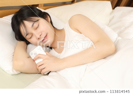 Young woman lying in bed and holding a smartphone 113814545