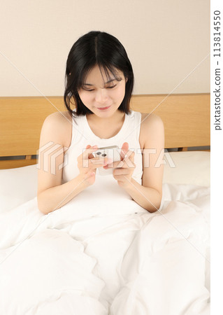 Young woman sitting in bed and looking at her smartphone Young woman sitting in bed and looking at her smartphone 113814550