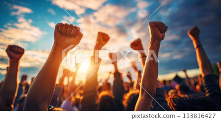 Raised fists of a crowd against a sunset sky 113816427