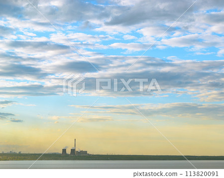 CHP and other plants stand on the shore of the lake in the evening under clouds in the sky 113820091