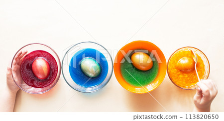 Hands of a girl child coloring festive Easter eggs with colorful dyes on the table at home 113820650