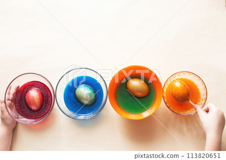 Hands of a girl child coloring festive Easter eggs with colorful dyes on the table at home 113820651