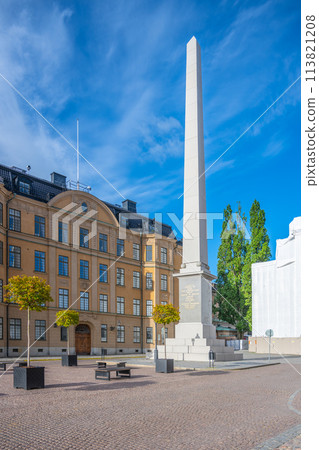The obelisk at Slottsbacken stands tall against a clear blue sky in Stockholm, with historic buildings flanking the sides and trees adding a touch of green. Sweden The obelisk at Slottsbacken stands tall against a clear blue sky in Stockholm, with historic buildings flanking the sides and trees adding a touch of green. Sweden 113821208