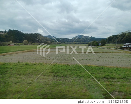 在陰雲密佈的天空下，村外的耕地外，一座新綠的山巒橫亙在村外。 113821268
