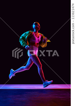 Dynamic image of sportive young girl in sportswear, jacket and headphones training, running on black background in neon light Dynamic image of sportive young girl in sportswear, jacket and headphones training, running on black background in neon light 113821474