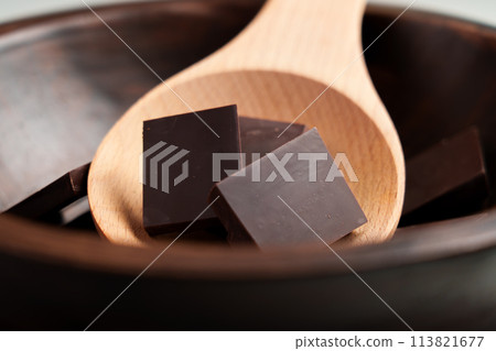 Pieces of dark chocolate from pure cacao ingredients in rustic bowl with wooden spoon 113821677