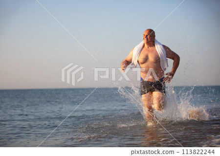 An elderly man runs along the beach. 113822244