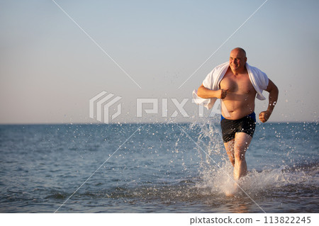An elderly man runs along the beach. 113822245